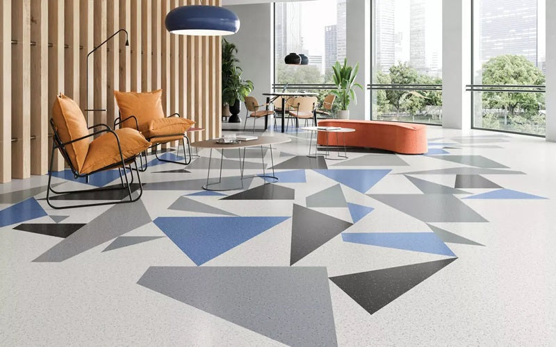 Tarkett Flooring a large room with floor-to-ceiling windows and a blue, grey and white geometric pattern on the floor, with 3 modern, orange chairs